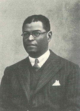 A black and white photograph of a black man wearing spectacles and a black pinstriped suit.